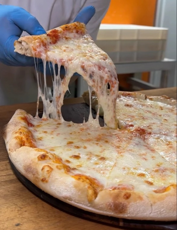 A slice of PIZAZA Margherita lifted from the pizza with a long mozzarella pull