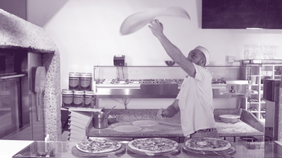 A PIZAZA chef spinning pizza dough in the kitchen, beside the brick oven